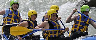 Five people rafting on river blue and yellow paddles.