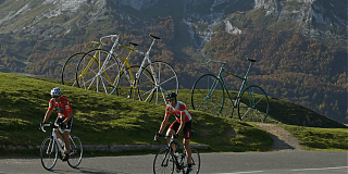 Men on bicycles with mountains and three bikes in background.
