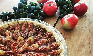 Fig tarte homemade, apples and grapes on table behind.