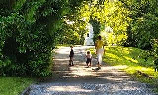 Mother and two children walking on gravel path through trees.
