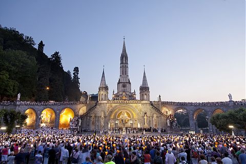 People holding candles outside lourdes church.