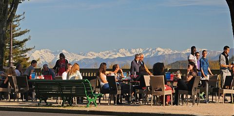 People sitting at tables outside with view of snow capped mountains in background.